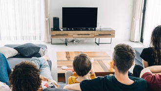 Famiglia guarda la TV di spalle seduta sul divano